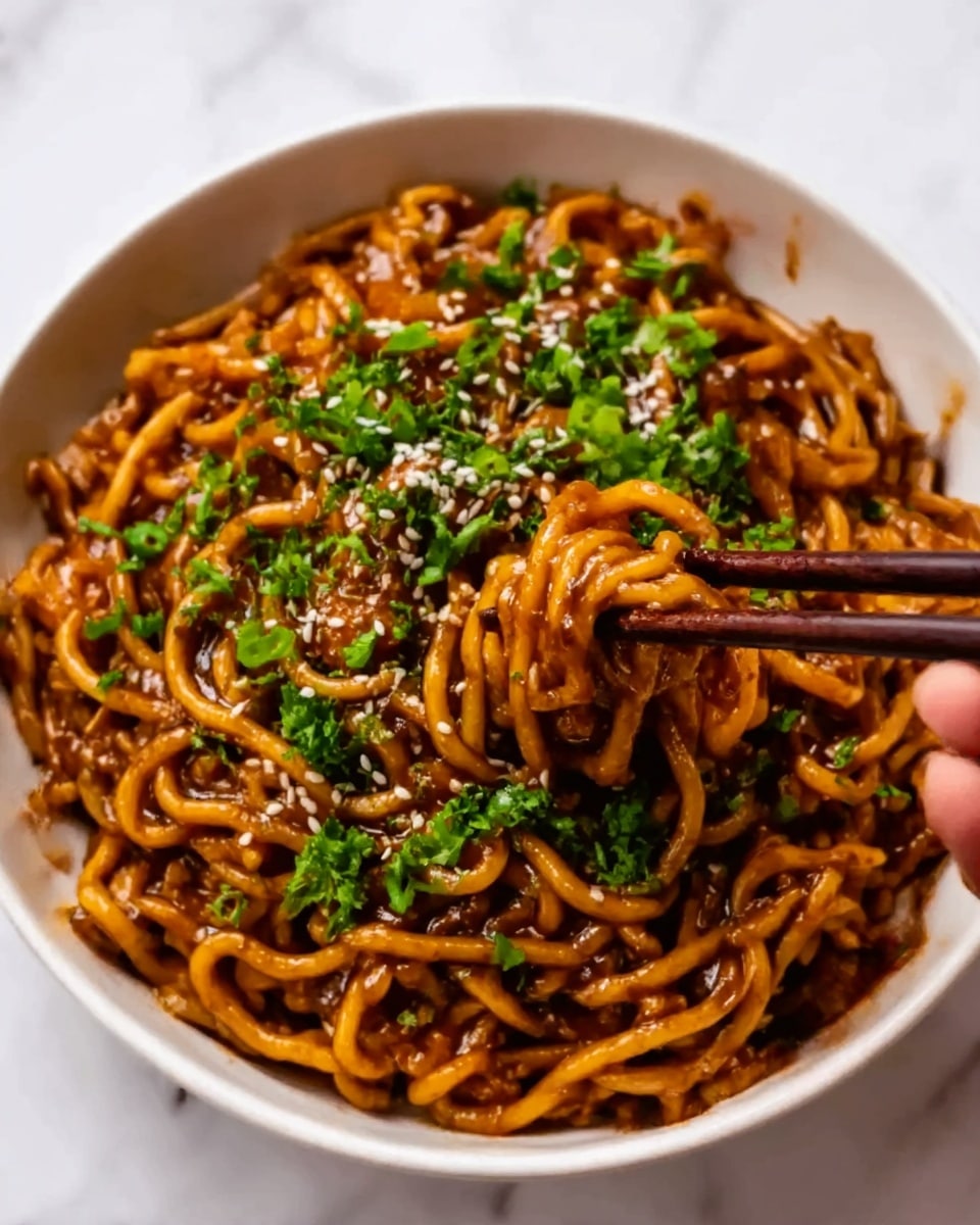 A close-up of a white bowl filled with curly noodles coated in a dark brown sauce. The noodles are mixed with small pieces of vegetables and topped with white sesame seeds. Bright green chopped herbs are scattered on top, adding color contrast. A woman's hand is holding dark brown chopsticks, lifting some noodles above the bowl. The scene is set on a white marbled surface. Photo taken with an iphone --ar 4:5 --v 7
