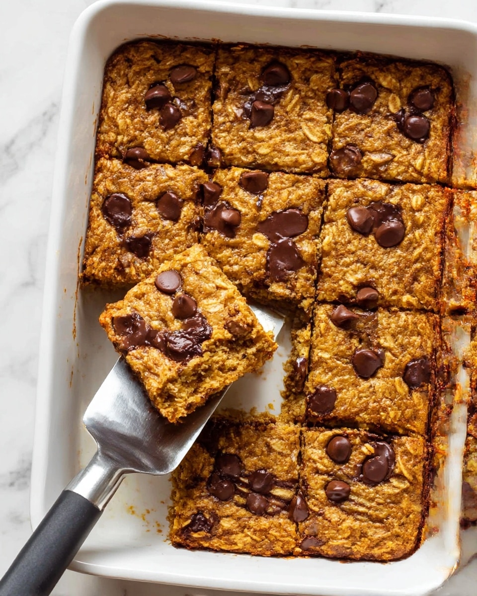 The image shows a white rectangular baking dish filled with a baked oatmeal cut into nine square pieces. The oatmeal has a golden-brown color with a slightly rough and moist texture, and is topped with dark chocolate chips scattered evenly across the surface. One piece is lifted slightly by a metal spatula with a black handle, revealing a soft inside layer that is lighter yellow compared to the top. The dish is placed on a white marbled surface with part of a folded brown cloth visible at the edge. photo taken with an iphone --ar 4:5 --v 7