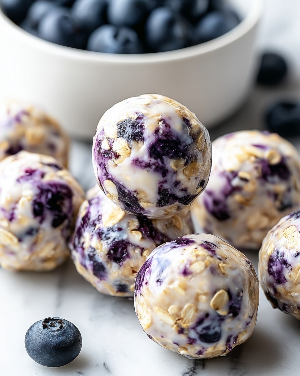 The image shows several round, bite-sized energy balls placed on a white marbled surface. Each ball has a creamy white base mixed with visible oats and dark purple-blue spots of blueberries, giving a speckled texture. The balls look slightly glossy, as if coated with a light moisture or syrup. A white bowl filled with fresh blueberries is visible in the background, blurred to keep the focus on the energy balls. The scene emphasises the natural mix of oats and blueberries in the snack. photo taken with an iphone --ar 4:5 --v 7