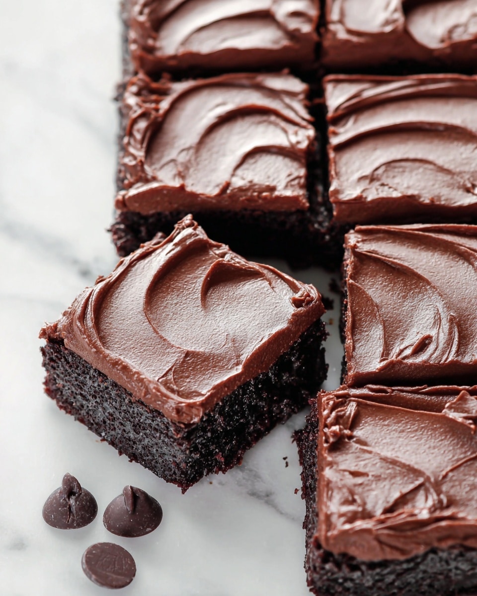 A tray of chocolate brownies cut into twelve square pieces is shown on a white marbled surface. Each brownie has two visible layers: a dark, rich, slightly crumbly base and a thick, glossy layer of smooth chocolate frosting on top with gentle swirls and curved textures. One brownie square is pulled slightly away from the tray, highlighting its thick frosting and moist cake below. Below the brownies, three whole chocolate chips rest on the white marbled surface. photo taken with an iphone --ar 4:5 --v 7
