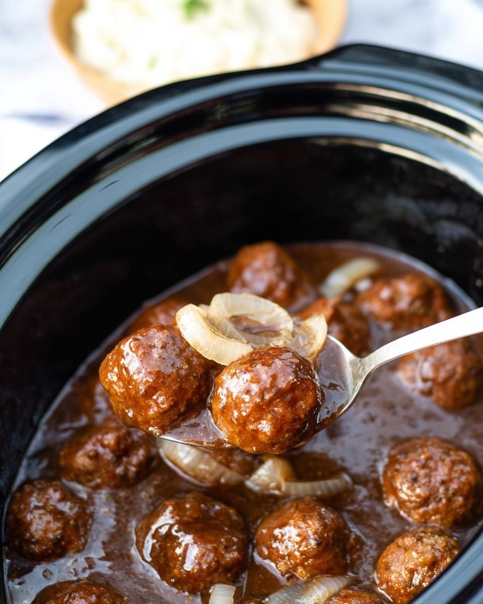 A spoon holds six small brown meatballs covered in a glossy dark brown gravy with translucent cooked onion slices on top, all inside a black slow cooker filled with more meatballs and thick gravy which has a slightly shiny surface; in the background, a blurred white bowl with a light creamy topping is partially visible, set on a white marbled surface. photo taken with an iphone --ar 4:5 --v 7