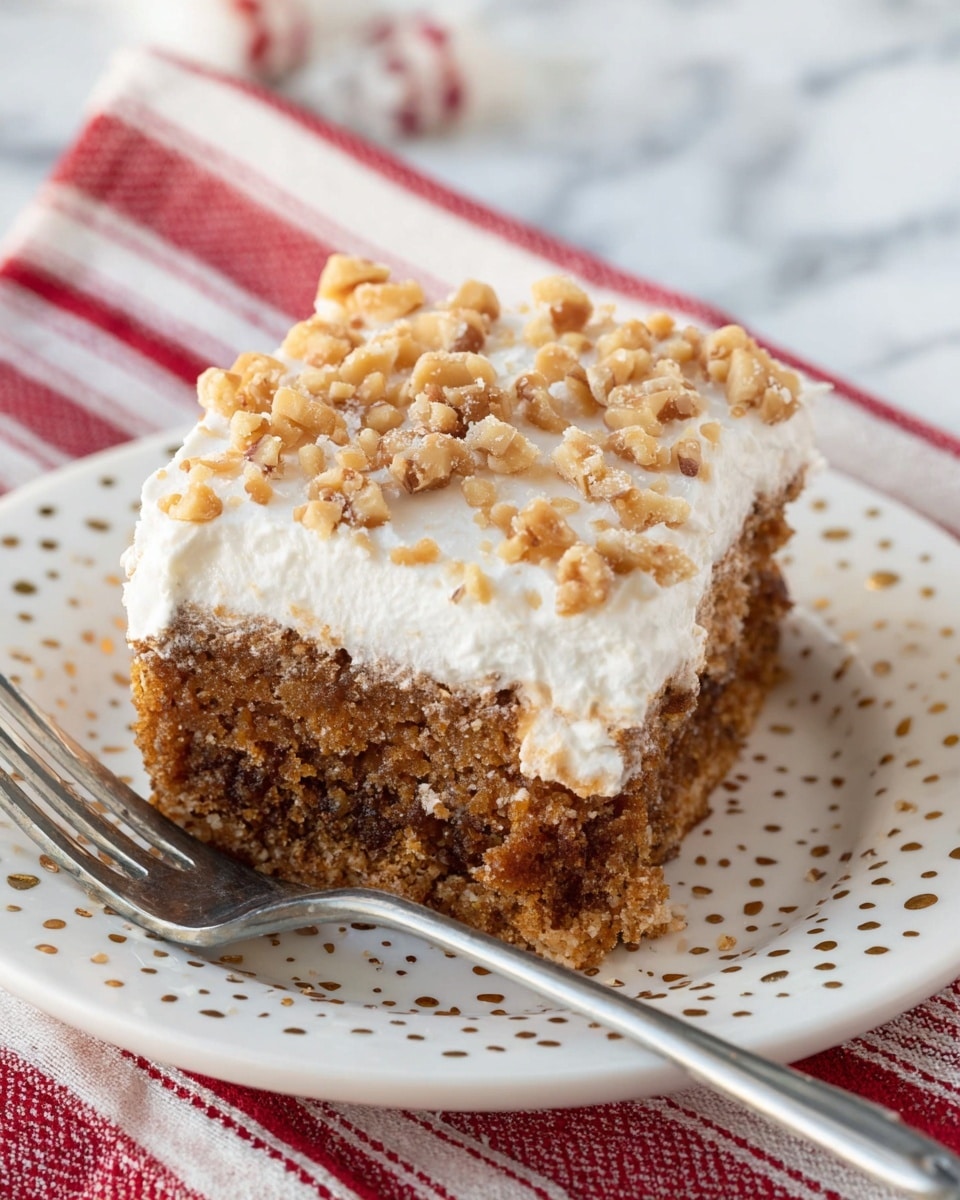 A close-up of a square piece of cake sits on a white plate with small gold dots near the edges. The cake has two clear layers: the bottom layer is thick and looks moist with a dark brown, slightly crumbly texture, while the top layer is thick and fluffy white frosting covered generously with small, chopped light brown nuts. The plate rests on a red and white striped cloth, against a white marbled surface, and a silver fork lies beside the cake on the plate. photo taken with an iphone --ar 4:5 --v 7