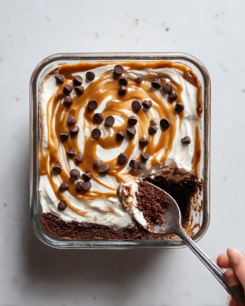 The image shows a square glass dish with three visible layers of dessert. The bottom layer is dark brown and looks like dense chocolate cake or brownie. The middle layer is thick white cream, spread evenly. On top, there is a swirl of light brown caramel sauce spread unevenly, adding texture and shine. Scattered on the cream and caramel are medium-sized dark chocolate chips, giving a contrast in color and shape. A spoon is inserted into the right side of the dish, with some chocolate dessert on it, and a woman's hand is holding the spoon. The dish rests on a white marbled textured surface. Photo taken with an iphone --ar 4:5 --v 7