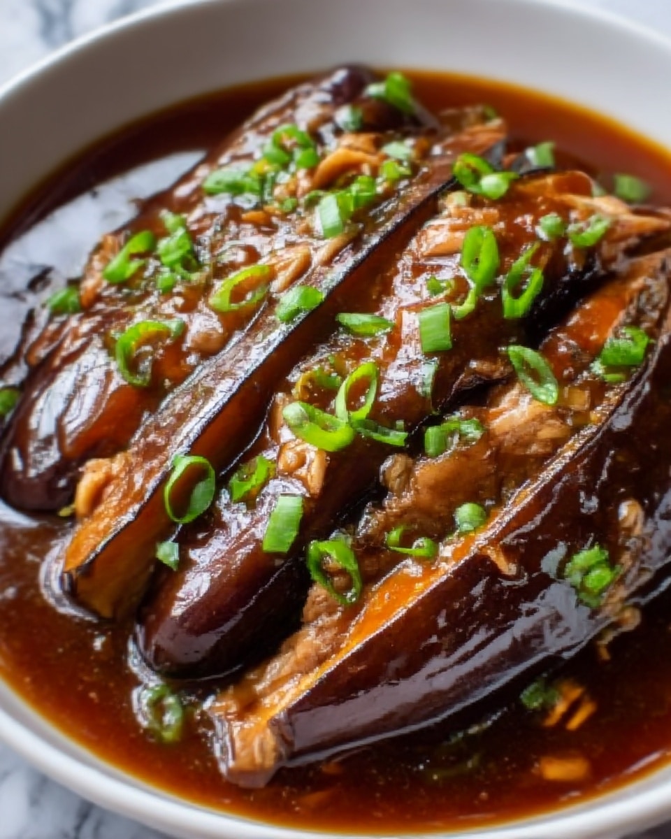 A close-up of a dish with three thick slices of glossy, dark brown cooked eggplant covered in a shiny brown sauce with small chopped green onions sprinkled on top. The eggplants are arranged side by side in a white bowl, and the sauce pools around them, adding a rich, moist texture. The background shows a white marbled surface. The photo taken with an iphone --ar 4:5 --v 7