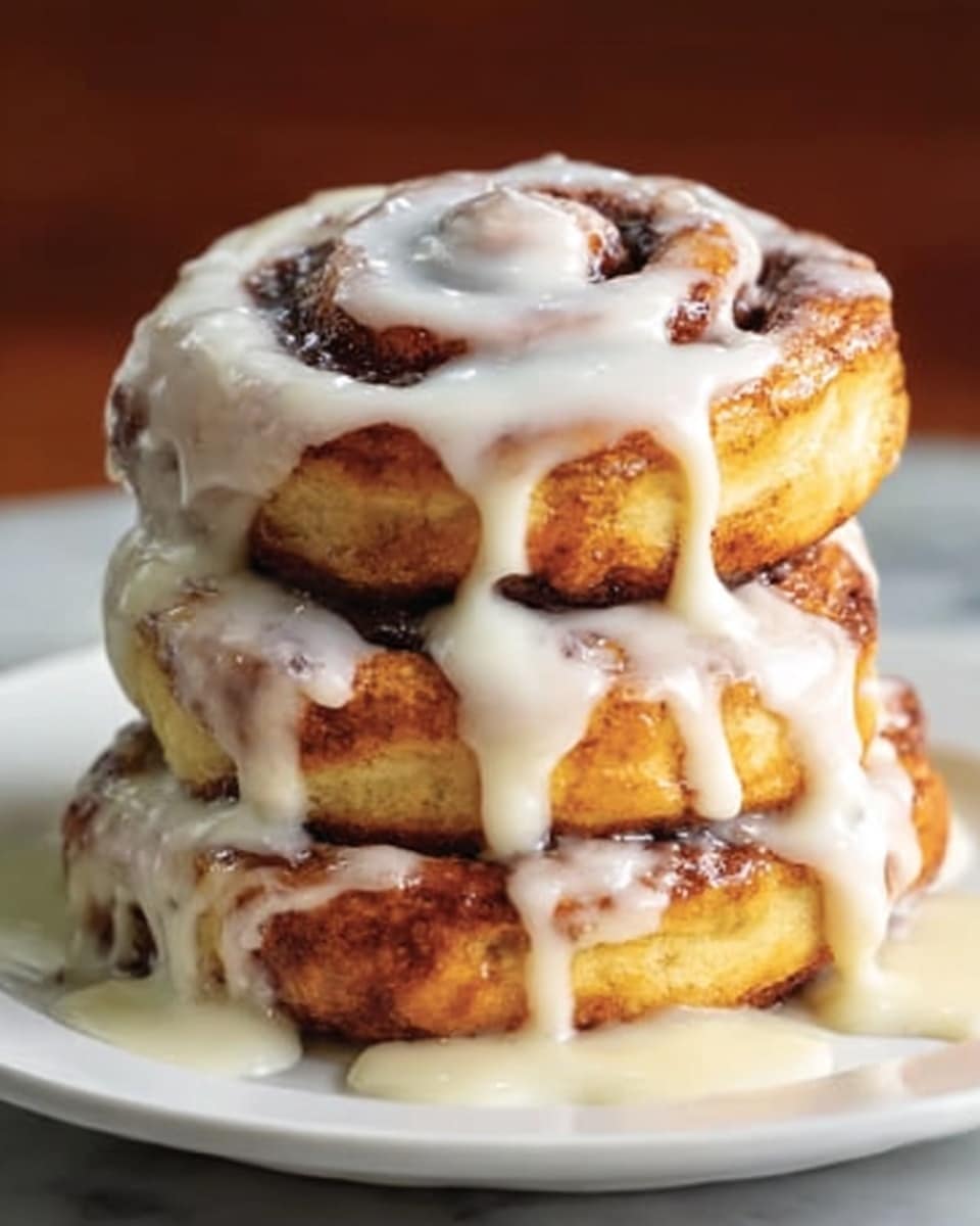A stack of three thick, golden-brown cinnamon rolls sits on a white plate, each roll showing swirls of dark cinnamon filling. The rolls are soft and slightly shiny, with a creamy white glaze slowly dripping down the sides and pooling around the base. The background features a white marbled texture, adding brightness to the warm tones of the rolls. Photo taken with an iphone --ar 4:5 --v 7